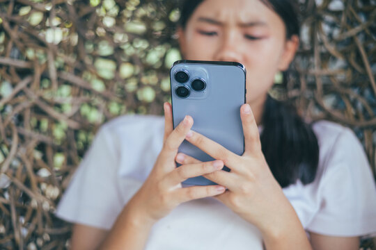 Worried and stressed Asian teenager girl holding smartphone looking at screen with anxious expression. Concept of cyberbullying, social media peer pressure, smartphone digital addiction, and youth men
