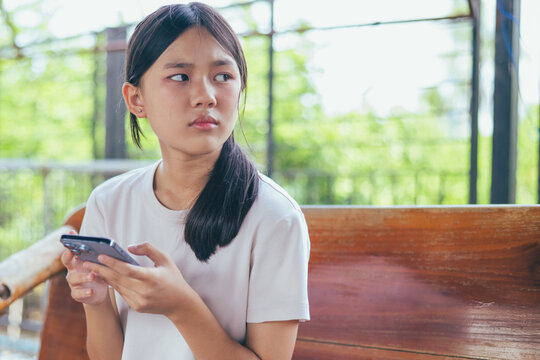 Worried and stressed Asian teenager girl holding smartphone looking at screen with anxious expression. Concept of cyberbullying, social media peer pressure, smartphone digital addiction,