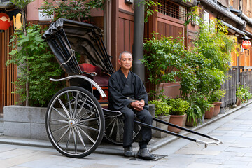 Obraz premium Rickshaw Puller Resting on Stone Street Between Rides in Traditional Attire in Urban Environment