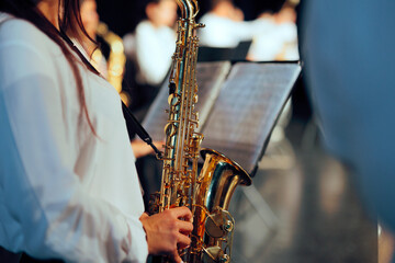 Obraz premium Female Saxophonist Reading Music Sheet During Live Concert Performance. Close up of girl playing brass saxophone next to music stand indoors