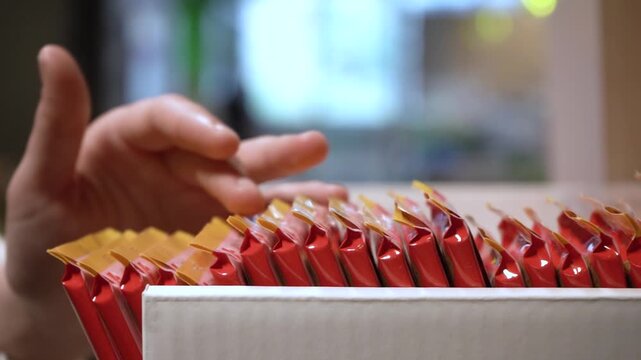 A Close-Up of a Hand Sorting Colorful Packaging in a Box, Showcasing Organized Rows of Snack Products in a Bright Environment