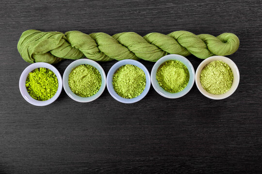 Different varieties matcha powder in small ceramic bowls arranged near a green fabric textile. Overhead view of organic Japanese green tea ingredient for healthy drink and detox beverage preparation