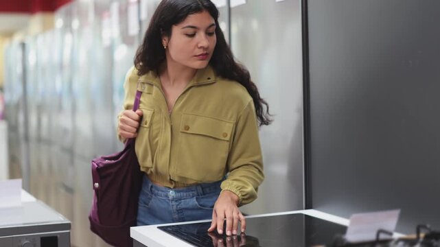 Beautiful young woman chooses and buys ceramic hob in local hardware store. High quality 4k footage