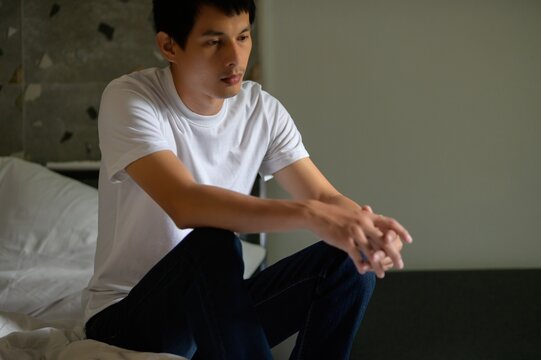 Thoughtful Young Man Sitting on Bed in Quiet Room Reflection