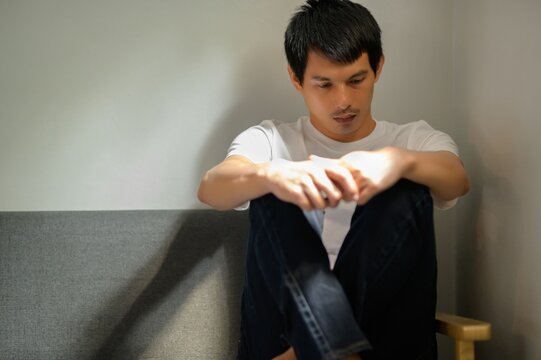 Young Man in Casual Attire Sitting Alone on a Sofa in Soft Light
