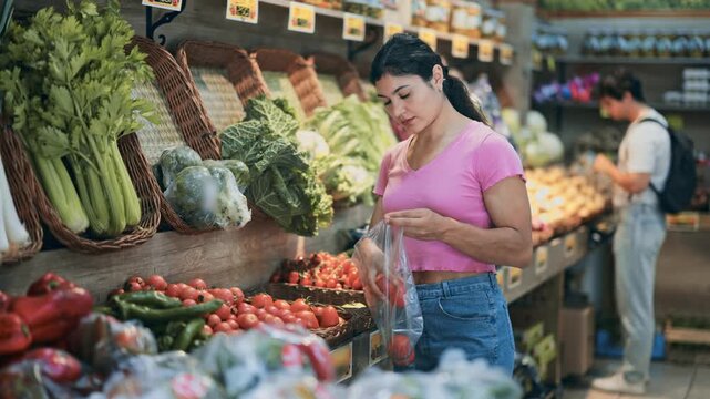Woman buys ripe red tomatoes in a supermarket. European woman stands near a vegetable counter and holds tomatoes in her hands, examines them and chooses them to cook dinner. High quality 4k footage