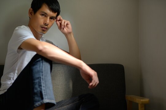 Thoughtful Young Man Sitting in Dimly Lit Room with Neutral Background