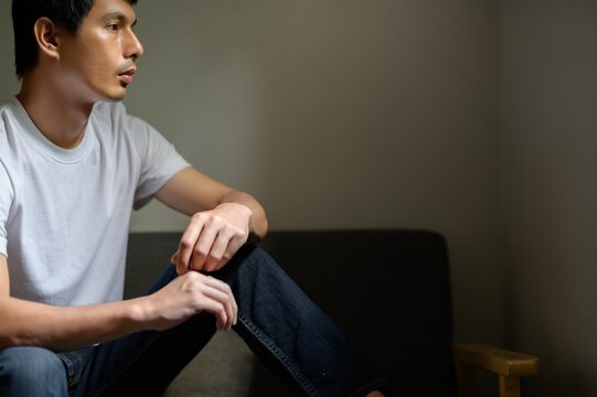 Thoughtful young man sitting in low light with serious expression