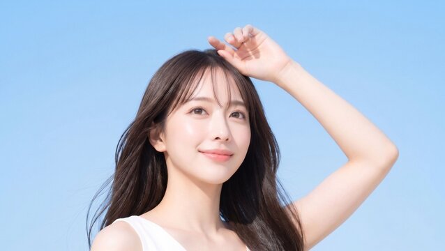 青空を背景に腕を上げて日差しを感じながら微笑む若い日本人女性の爽やかなUVケア・スキンケア美容ポートレート