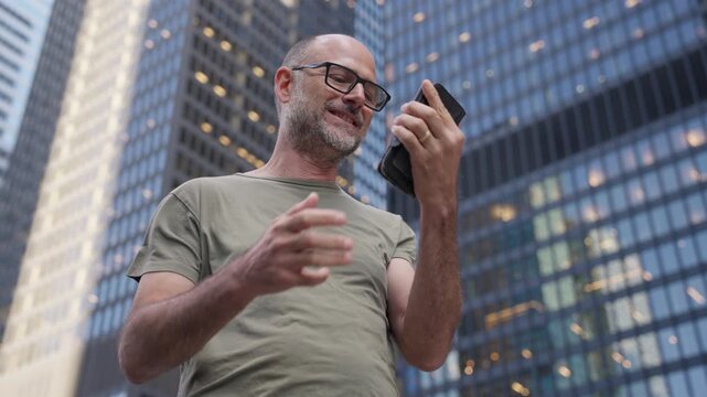 Man smiles while talking on a smartphone, ends the call and looks pleased in a financial district, Slow Motion