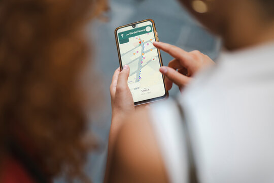 Two lost tourists use a smartphone navigation app to find directions in the city. Close-up of hands holding a mobile phone with a digital map displaying a route.