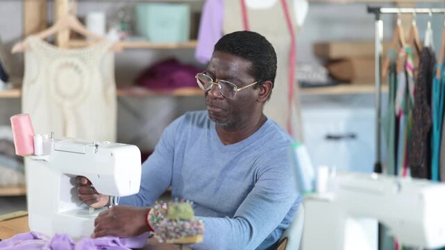 Male clothing designer stitching fabric on sewing machine in studio 