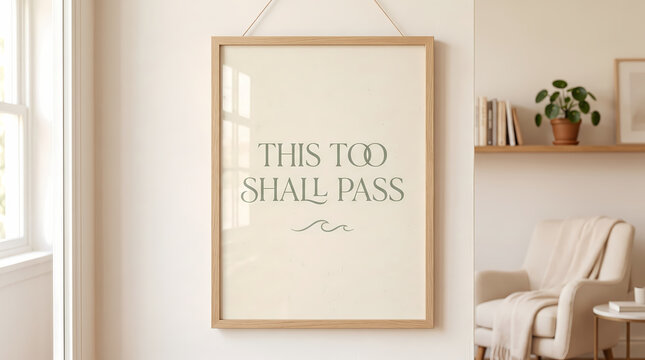 Vertical wooden frame hanging on a beige wall displays an inspirational quote reading this too shall pass with a small wave icon printed in a stylish elegant sage green font