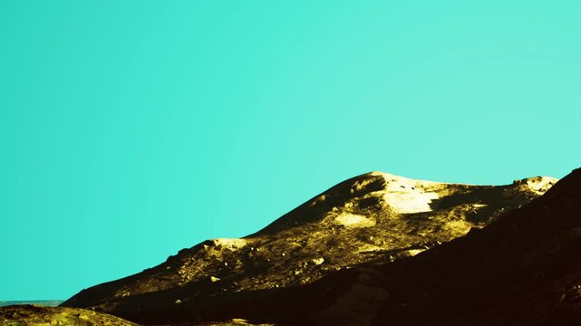 The scene shows mountains with rugged terrain and a clear blue sky in the background. The sunlight highlights the features of the hills and creates shadows.