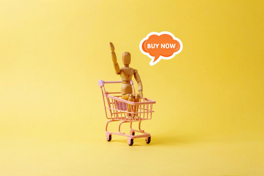 Wooden Mannequin in Shopping Cart with Buy Now Speech Bubble for Online Shopping Concept