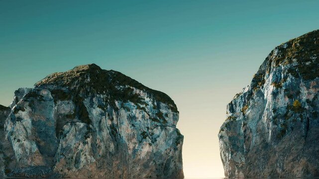 Two large rocks stand tall against a clear blue sky. The sun is setting low, creating a warm glow behind the rocks. The scene shows a natural landscape without any people or buildings.