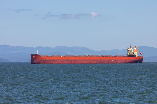 Large red cargo ship sailing on the Columbia River near Astoria, Oregon, USA, towards the Pacific Ocean, representing global shipping, logistics and international trade