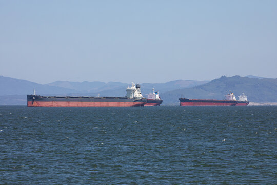 Multiple cargo ships sailing on the Columbia River near Astoria, Oregon, USA, towards the Pacific Ocean, representing global shipping, logistics and international trade