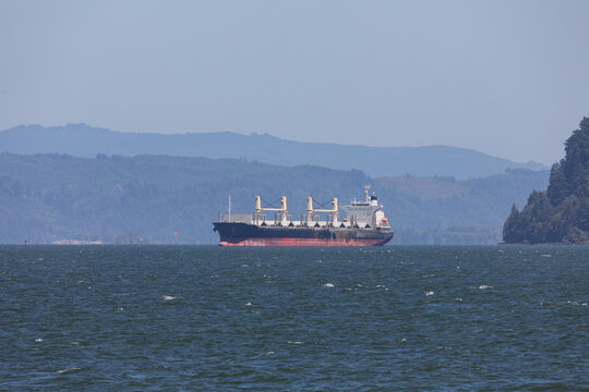 Geared bulk carrier sailing on the Columbia River near Astoria, Oregon, USA, towards the Pacific Ocean, representing global shipping, maritime logistics and international trade