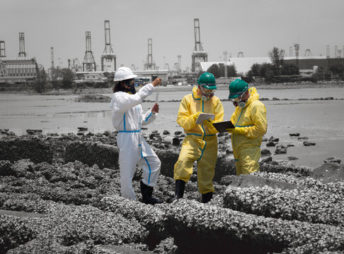 Scientists in chemical protective suits are at a water passage, collecting water samples and analyzing data on laptops to monitor pollution and contamination in the industrial area.
