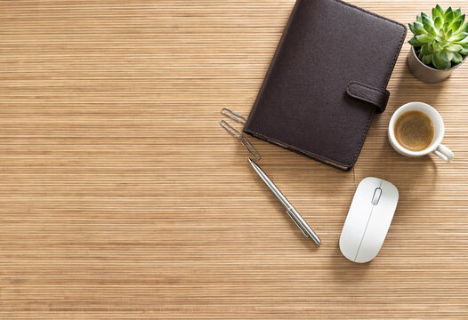Top view of office desk with notebook, pen, computer mouse, coffee and succulent