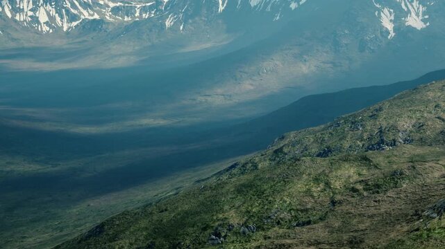 Mountains stretch across the landscape with shadows creating contrast. Green hills and rocky areas are visible under clear skies. The scene captures the natural beauty of the outdoors.