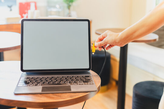 Woman's hand plugging charging cable into a tablet in cafe background.