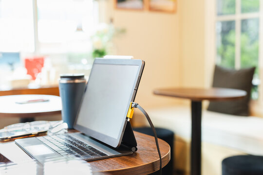 Laptop with charging cable and reusable travel mug for a remote work lifestyle.