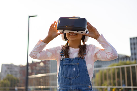 A young Caucasian girl wearing a VR headset and headphones is immersed in a virtual world outdoors