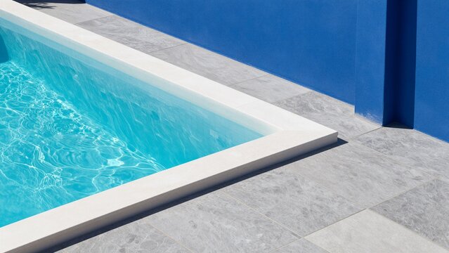 Clear turquoise water in a modern pool with white stone coping and grey tiled deck, set against a bold blue wall.