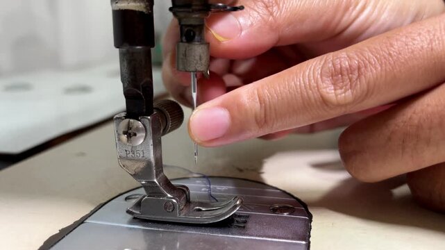 female tailor removing or replacing a needle from an industrial sewing machine in a workshop