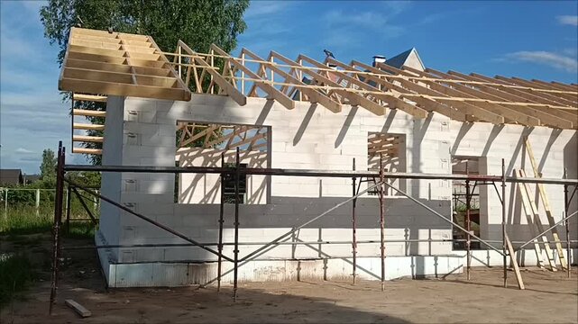 Wooden roof rafter installation on aerated concrete block walls of a house under construction with metal scaffolding.