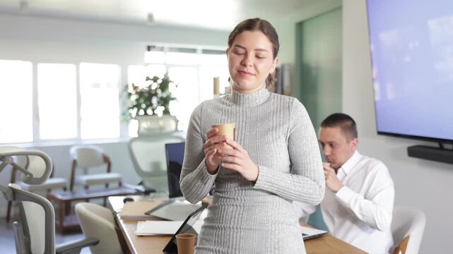  Young woman drinks coffee during break while working in office