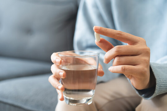 Sick, asian young woman, girl hand holding pill, painkiller medicine from stomach pain, headache, pain for treatment, take drug or vitamin and glass of water at home, pharmacy and health care concept.