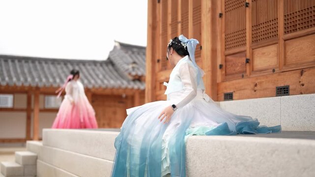 Woman in flowing traditional dress moves gracefully. She pauses beside a wooden building, smiling softly. Her gown sways gently with each step. The scene evokes peaceful tradition and cultural grace