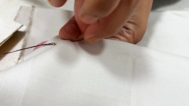 Close up of a female artisan hand sewing a manual baste stitch on fabric with needle and thread