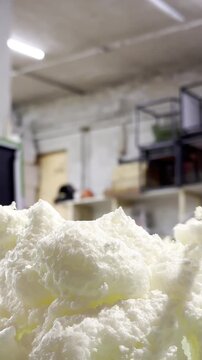 Worker using tool to shape polyurethane foam sealant in construction shop. Industrial repair process using white insulation foam for wall gap filling and sealing.