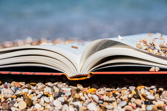 Closeup open book resting on a rocky beach by the sea, capturing a peaceful summer holiday atmosphere with relaxation, reading, and coastal nature