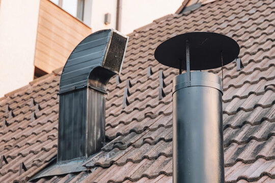 Modern metal ventilation duct and chimney stack on a tiled residential rooftop, providing exhaust and air circulation