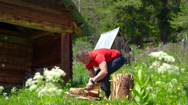 A cinematic wide shot of an athletic male hiker gathering chopped firewood logs into his arms and carrying them into a wooden banya.