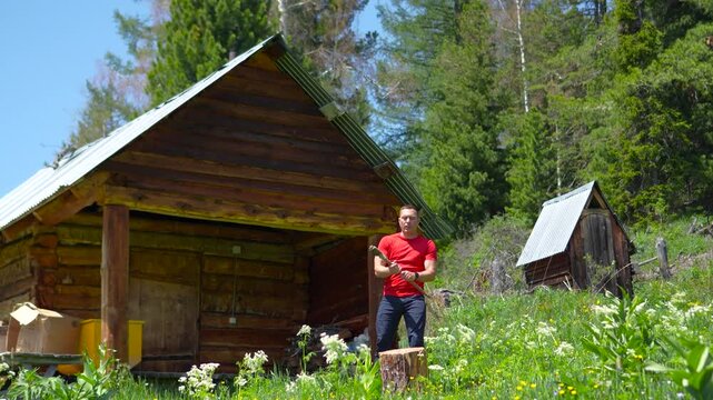 A cinematic video of an athletic man grabbing an axe, slinging it over his shoulder, and starting to chop a large firewood log in Altai.
