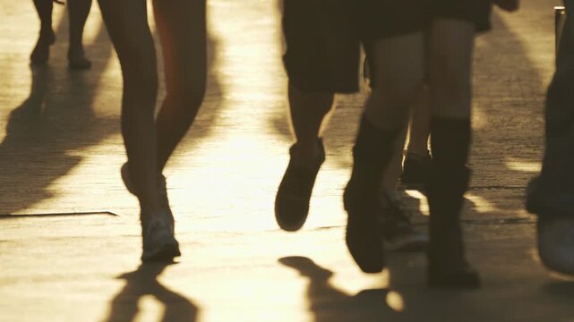 The silhouettes and shadows of people walking along the street are illuminated by the warm golden light of the setting sun, conveying the movement and atmosphere of an evening stroll.