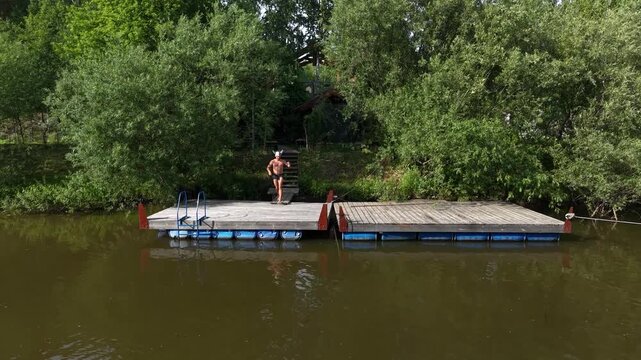 A cinematic wide shot of an athletic shirtless man running from a wooden banya sauna and jumping into a mountain river in Altai.