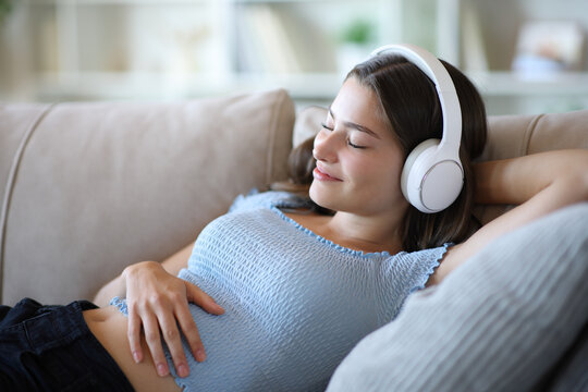 Satisfied teenage girl relaxing on a couch listening music