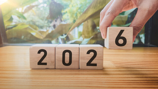 Year formation wooden blocks spelling 2026 with hand placing block and foliage sunlight background