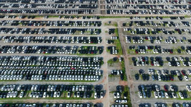 Aerial drone photograph of an automotive storage facility packed with new vehicles, representing inventory accumulation, manufacturing slowdown, economic pressure, and global market uncertainty. 4k.
