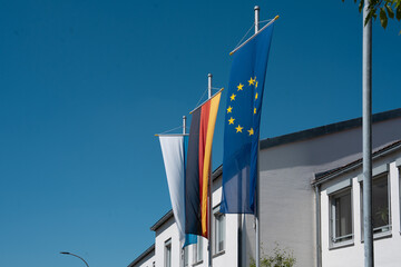 Bavarian, German and European Union flags on flagpoles in front of office building on sunny day in Germany