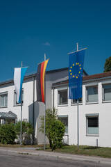 Bavarian, German and European Union flags on flagpoles in front of office building on sunny day in Germany