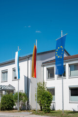 Bavarian, German and European Union flags on flagpoles in front of office building on sunny day in Germany