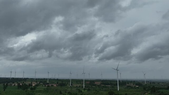 Drone perspective of a large wind farm beneath turbulent skies, illustrating the balance between renewable power, extreme weather, climate resilience, and long term environmental sustainability. 4k.
